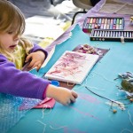 All of us have the urge to create and play. The artwork created by this girl is a song and dance of playful colour and textures. Getting ready to create, a mother and child explore the materials they could make an image with. Photo by Bronwyn Holmes.